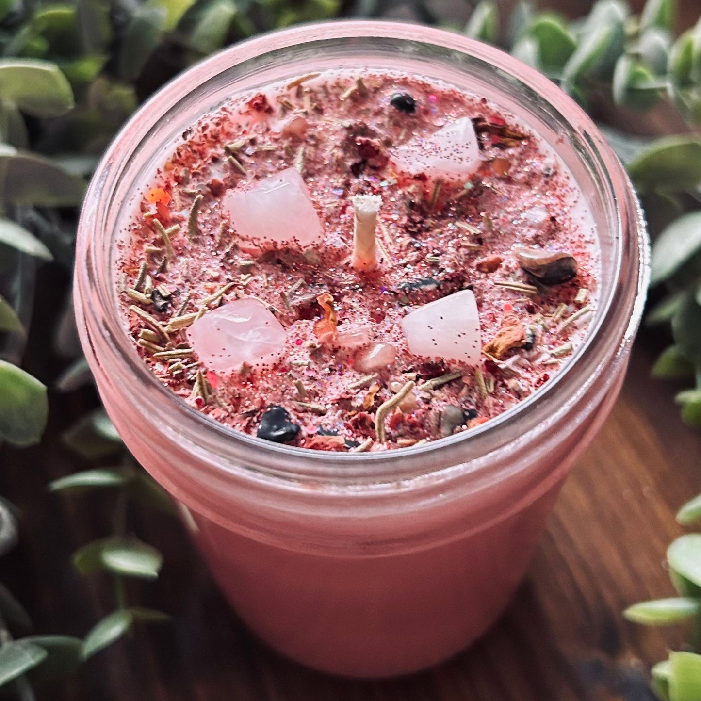 Pink confidence spell candle with rose quartz crystal, rosemary, roses, and glitter in a glass jar.