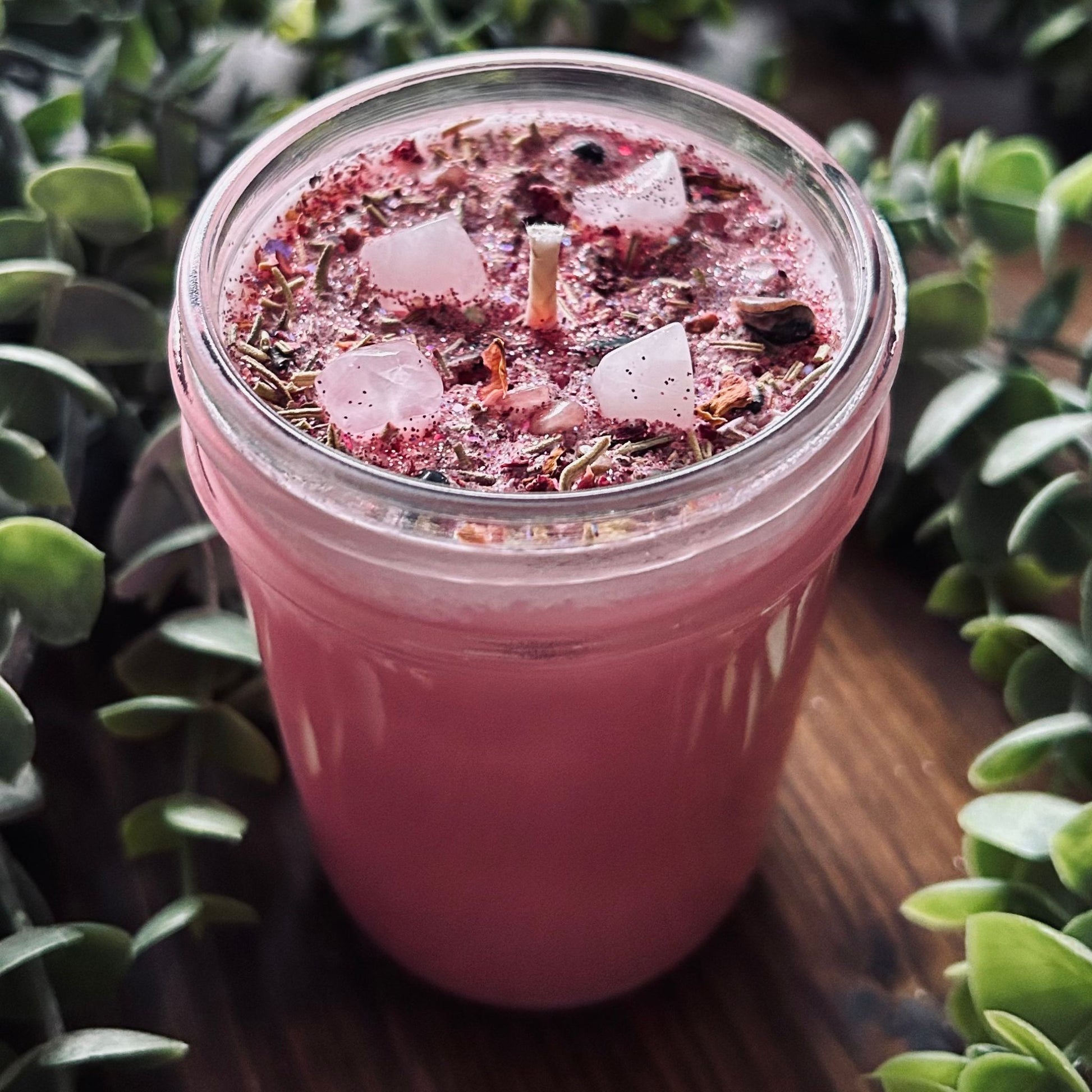 Pink confidence spell candle with rose quartz crystal, rosemary, roses, and glitter in a glass jar.