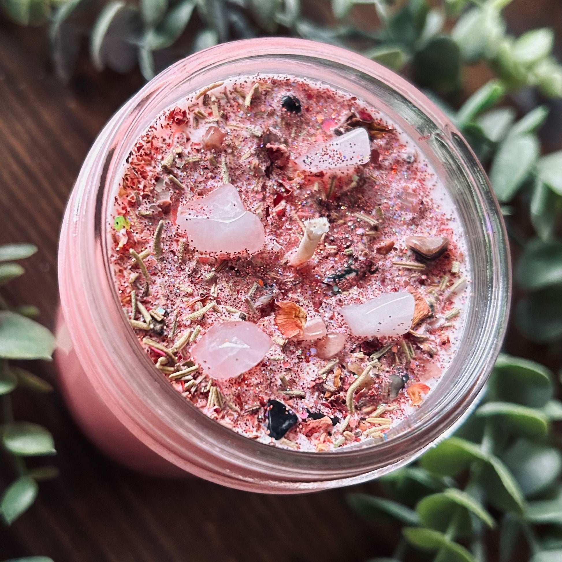 Pink confidence spell candle with rose quartz crystal, rosemary, roses, and glitter in a glass jar.