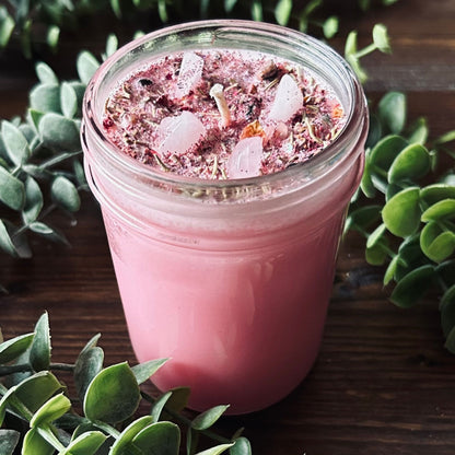 Pink confidence spell candle with rose quartz crystal, rosemary, roses, and glitter in a glass jar.