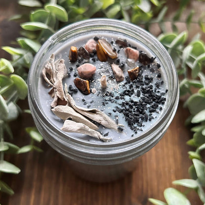 Silver intention candle that is decorated with gold tigers eye crystal, smokey quartz crystal, rhodonite crystal, protection salt, white sage, and witchy glitter to manifest goddess energy and power.