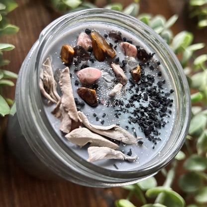 Silver intention candle that is decorated with gold tigers eye crystal, smokey quartz crystal, rhodonite crystal, protection salt, white sage, and witchy glitter to manifest goddess energy and power.