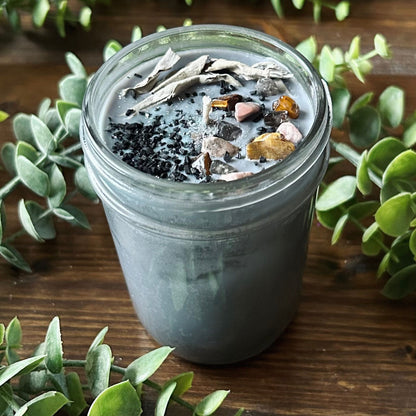 Silver intention candle that is decorated with gold tigers eye crystal, smokey quartz crystal, rhodonite crystal, protection salt, white sage, and witchy glitter to manifest goddess energy and power.
