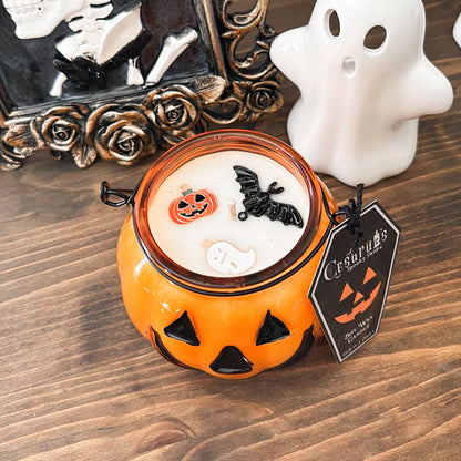 A Halloween candle in a jack o lantern that is decorated with a spooky bat, an autumn pumpkin, and a cute ghost.