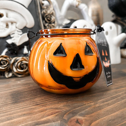 A Halloween candle in a jack o lantern that is decorated with a spooky bat, an autumn pumpkin, and a cute ghost.