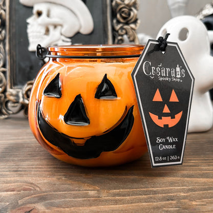 A Halloween candle in a jack o lantern that is decorated with a spooky bat, an autumn pumpkin, and a cute ghost.