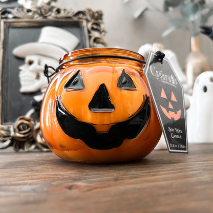 A Halloween candle in a jack o lantern that is decorated with a spooky bat, an autumn pumpkin, and a cute ghost.