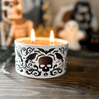 A gothic candle with a black and white swirl design that is decorated with a black skull, a raven, and a spooky bat.