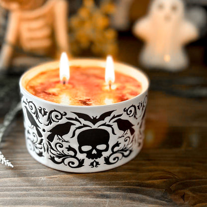 A gothic candle with a black and white swirl design that is decorated with a black skull, a raven, and a spooky bat.