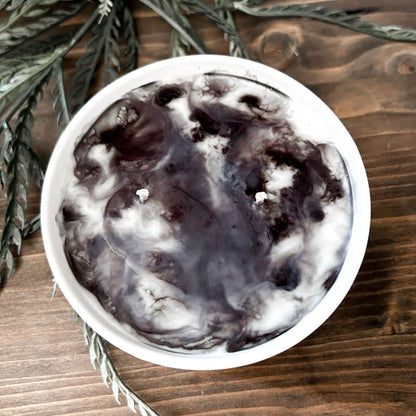 A gothic candle with a black and white swirl design that is decorated with a black skull, a raven, and a spooky bat.