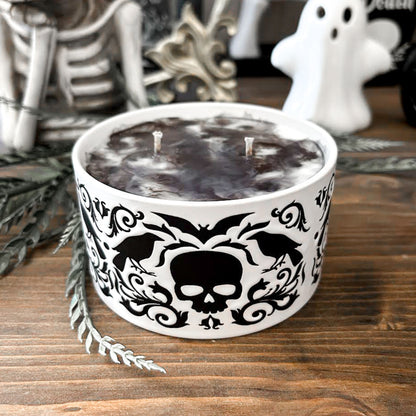 A gothic candle with a black and white swirl design that is decorated with a black skull, a raven, and a spooky bat.